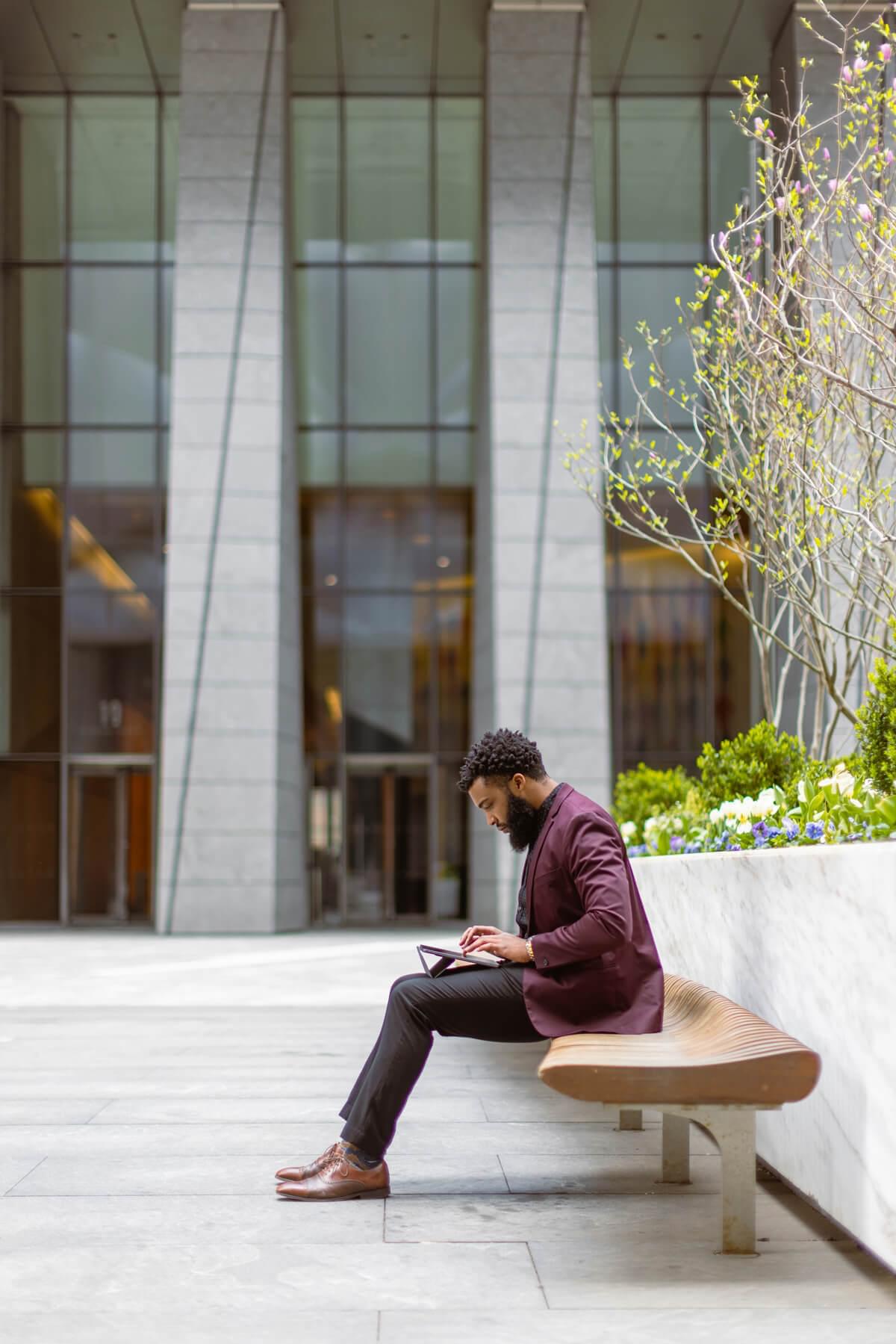 A well-dressed man works on his tablet outside a refined executive building.